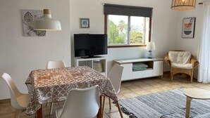 A dining area with a table set for four, a television, a window with a view, and a wicker chair.