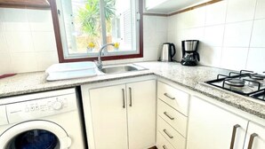 A compact kitchen with a washing machine, a coffee maker, and a stove.