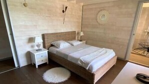 A bedroom with a wooden floor, a bed with white bedding, a nightstand with a lamp, and a round rug.