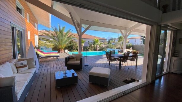 A covered outdoor area with a pool, wooden deck, and outdoor seating.