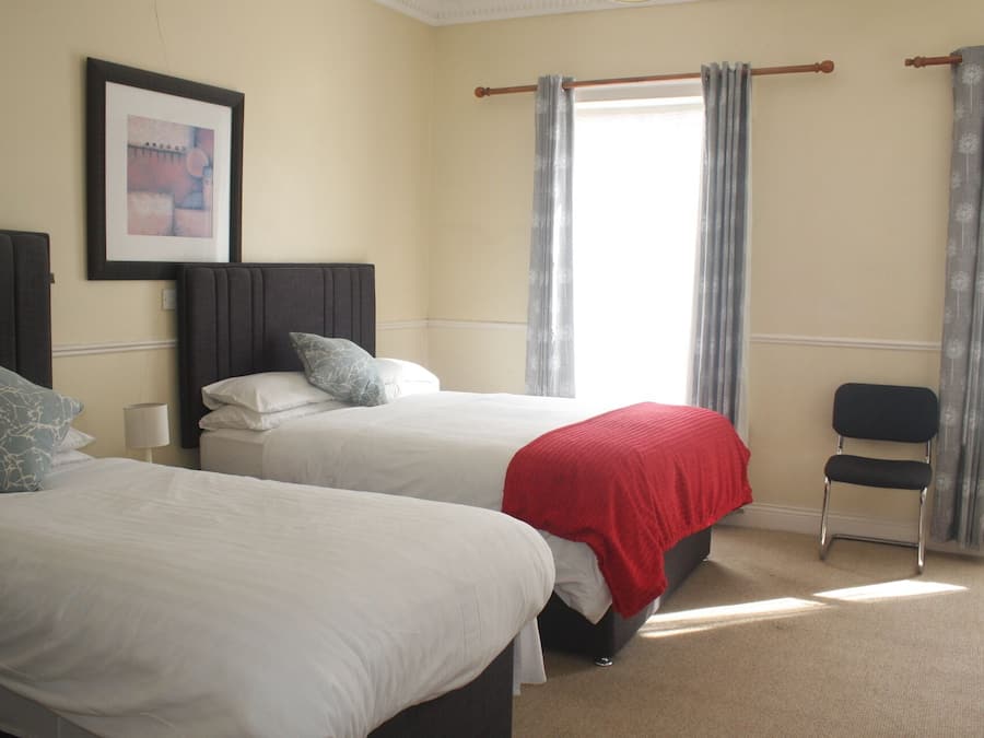 Une chambre d’hôtel avec deux lits, une chaise et un tableau encadré au mur.