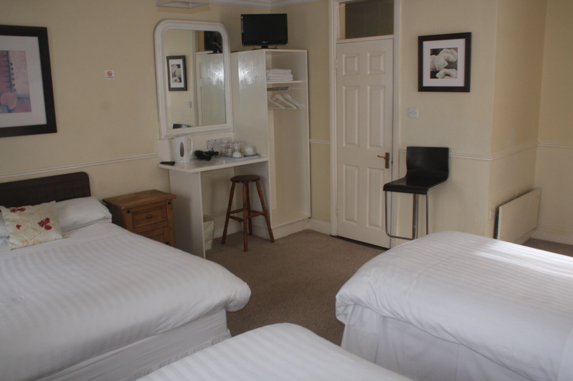 Une chambre d’hôtel avec deux lits, un bureau avec un miroir, une chaise et une armoire.