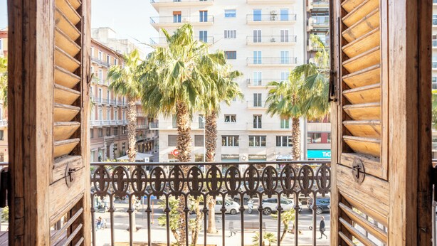 A balcony with wrought iron railings, overlooking a street with palm trees and multi-story buildings. - Bari LandLord 71 (Bari)