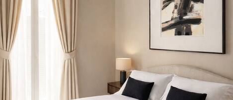 A hotel room with a bed, curtains, an air conditioning unit, a lamp, and a framed abstract painting on the wall.
