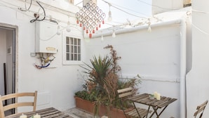 A small outdoor patio with wooden tables and chairs, a potted plant, and a hanging light fixture. - Bari LandLord 71 (Bari)