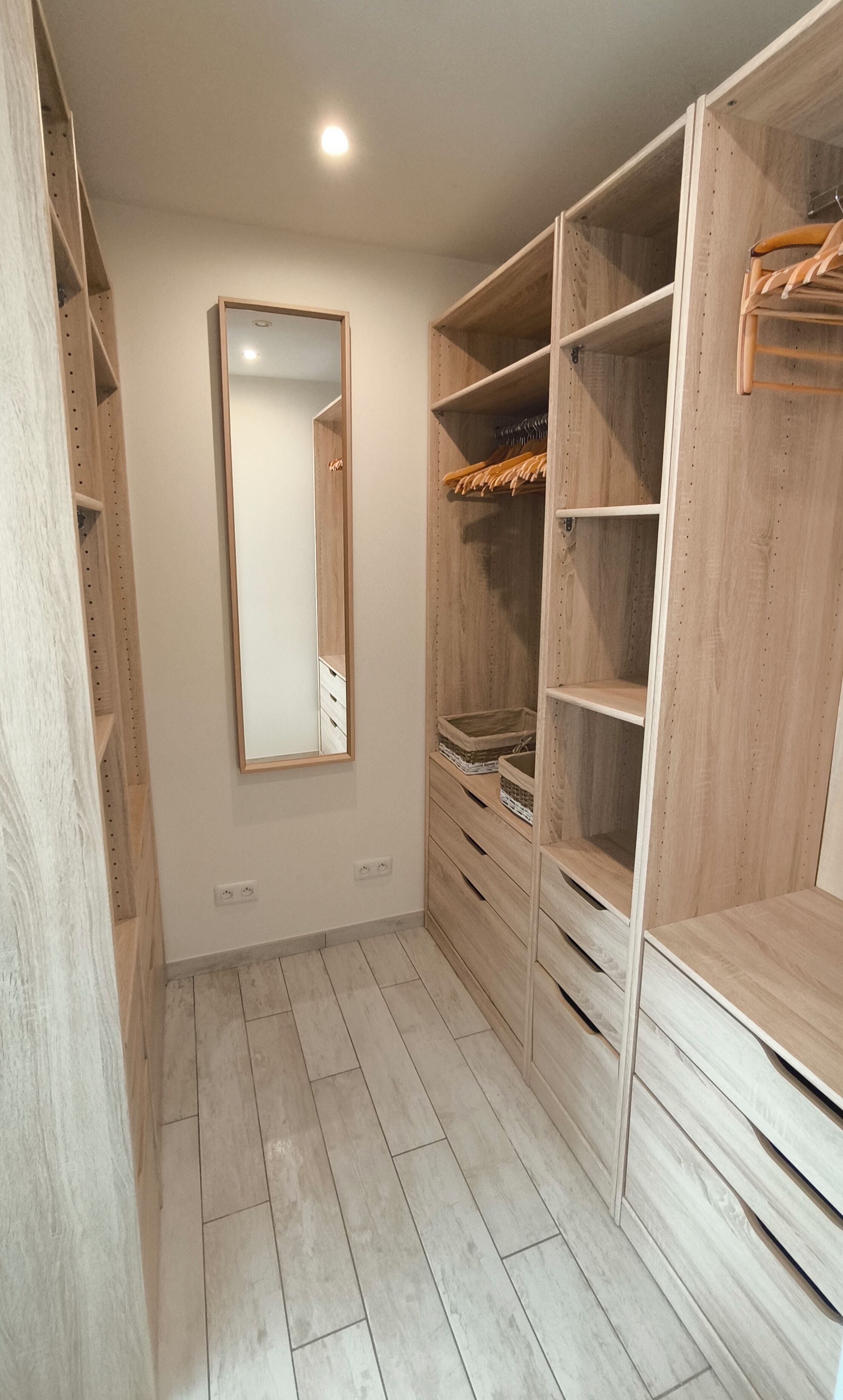 A walk-in closet with wooden shelving, a mirror, and a hanging rod.