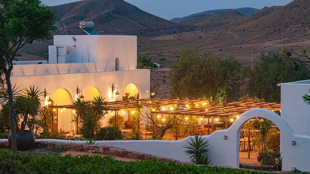 A building with arched windows and a covered outdoor seating area with string lights. - Finca Maltés San José (Nijar)