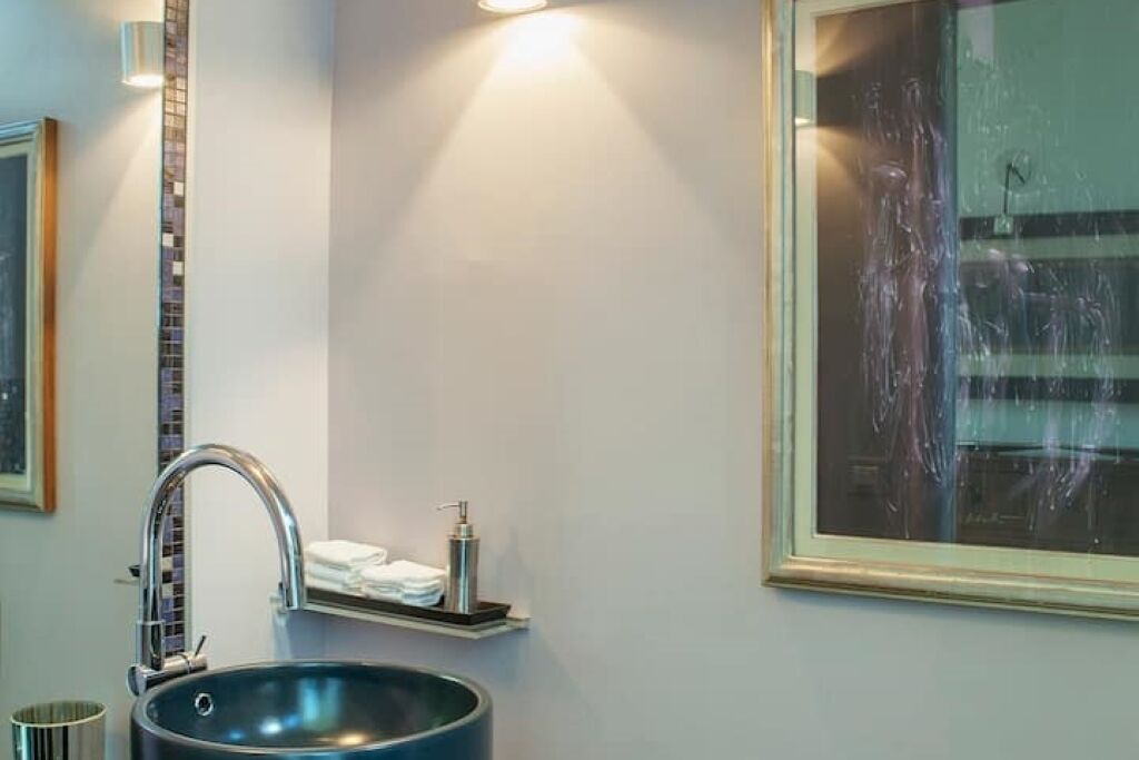 A bathroom with a large mirror, a modern faucet, and a sink.