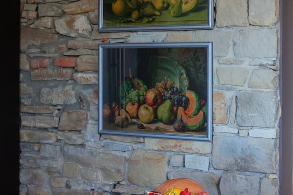A stone wall with two framed paintings of fruit.
