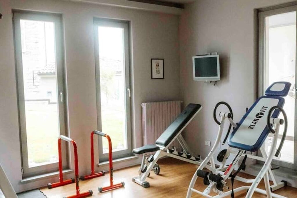 A gym with exercise equipment, a bench, and a television on the wall.