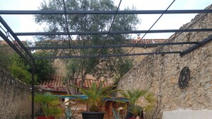 Un patio couvert avec deux chaises rouges, des plantes en pot et un mur en pierre.