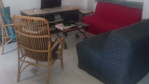 Un salon avec un plafond en bois, un canapé rouge, un fauteuil à motifs, un téléviseur et une petite table sur laquelle se trouvent des livres et une télécommande.