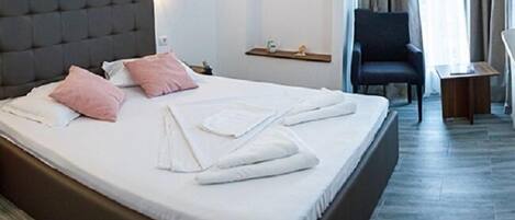A neatly made bed with white and pink pillows, a headboard, and a painting on the wall.