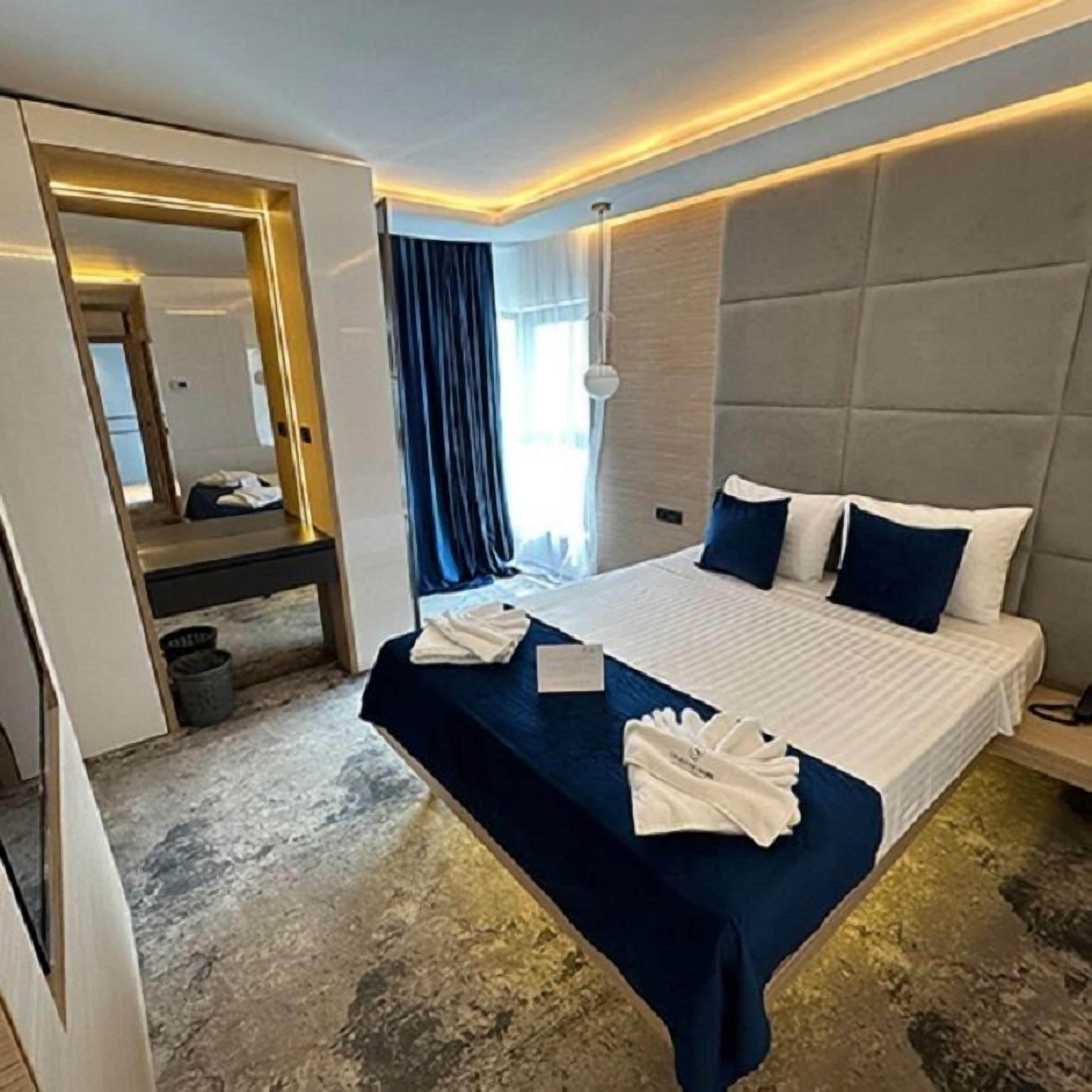 A modern hotel room with a large bed, a bedside table, a mirror, and a view of the outdoors.