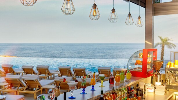 A bar with a view of the ocean, wooden lounge chairs, and various drinks.