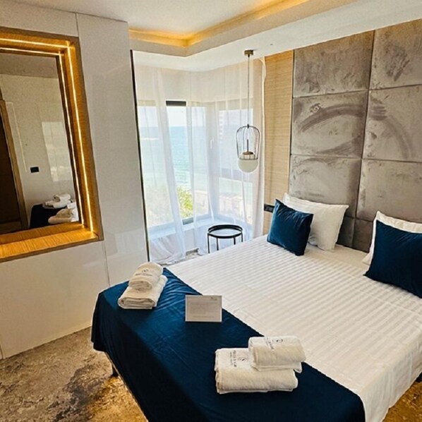 A hotel room with a bed, a bedside table, a mirror, and a view of the outdoors.