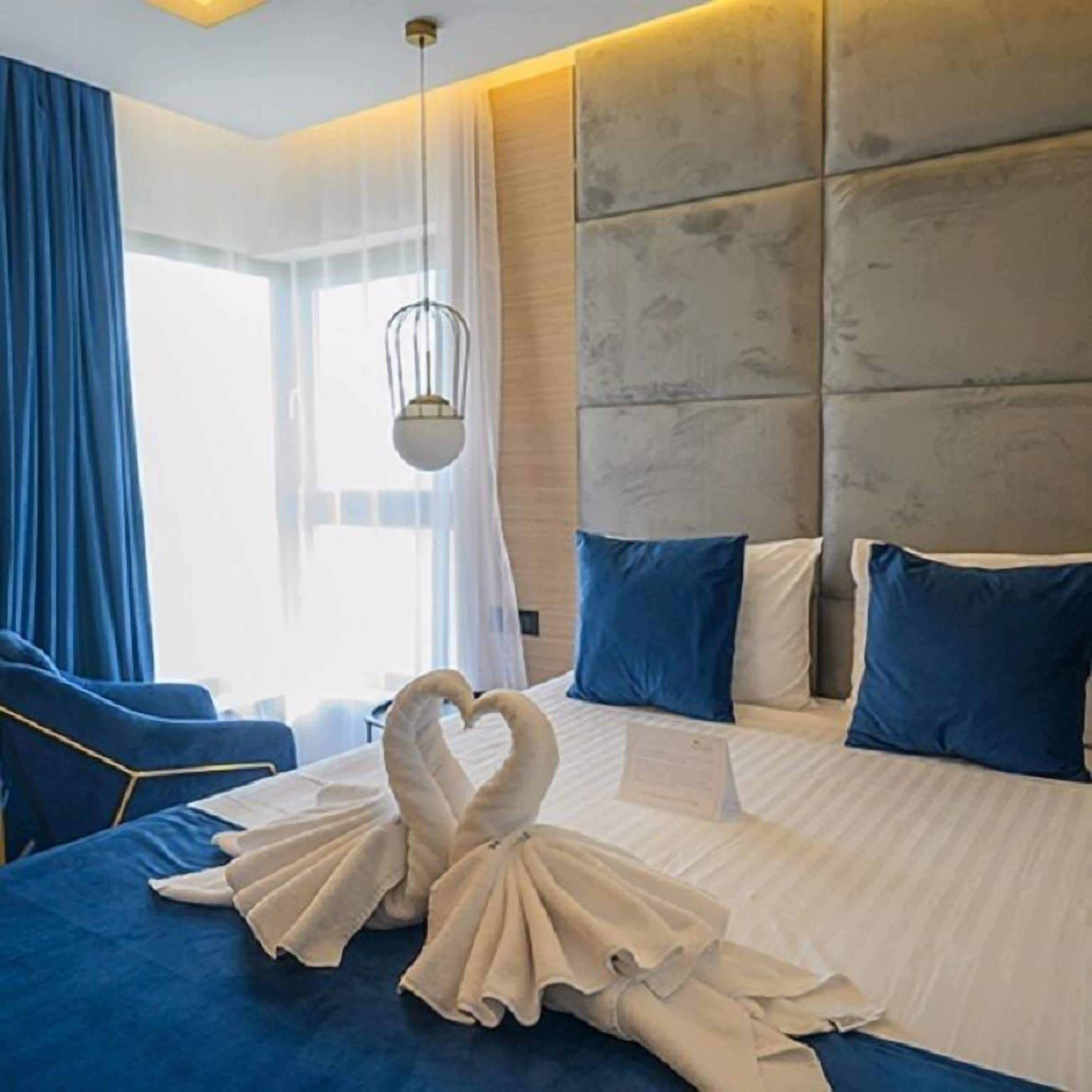 A hotel room with a large bed, blue and white pillows, and a heart-shaped towel arrangement on the bed.