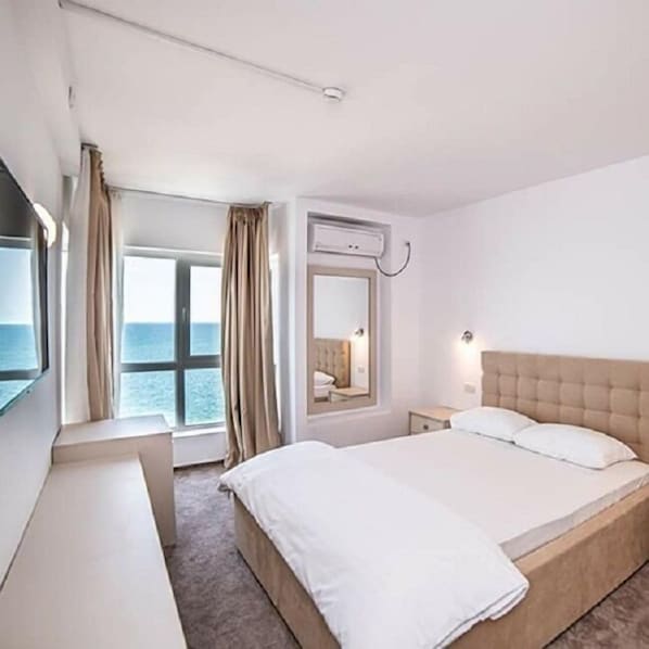 Habitación de hotel con una cama grande, una mesita de noche, un espejo y una ventana con cortinas.