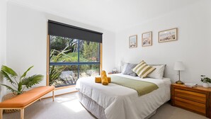 Una camera da letto con una grande finestra, un letto con cuscini, un comodino con una lampada e una panca con una pianta.
