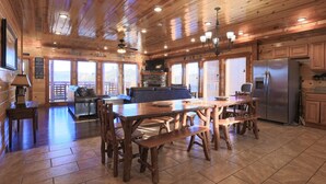 A wooden cabin interior with a dining area, kitchen, and a fireplace.