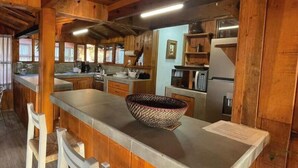 A rustic kitchen with wooden walls, a central island with a woven bowl, bar stools, and modern appliances. - Renovated and Harmonious Cabin in Valle de Bravo (Valle de Bravo)
