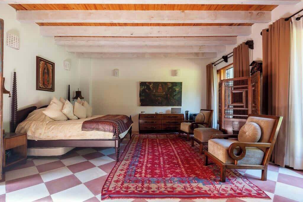 A bedroom with a bed, a dresser, a chair, a red patterned rug, and a painting on the wall.