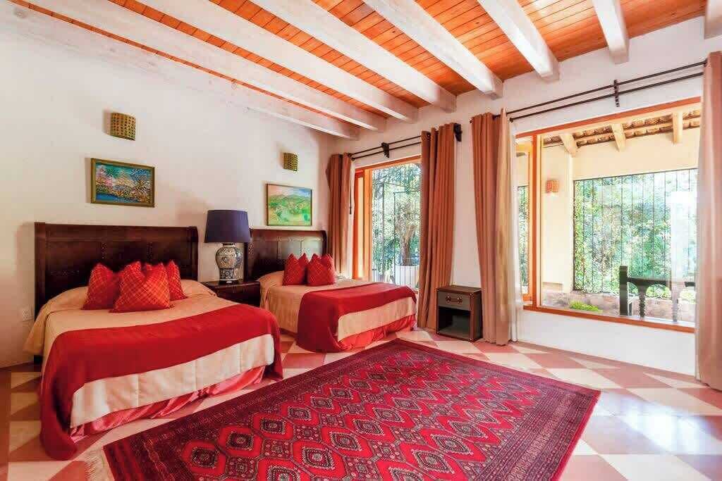 Un dormitorio con dos camas, un tapete grande con estampado, vigas de madera en el techo y vistas por una ventana.