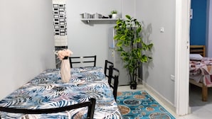Ett litet, välordnat sovrum med en säng, en stol, ett bord med en vas med blommor, en hylla med dekorativa föremål och en krukväxt.
