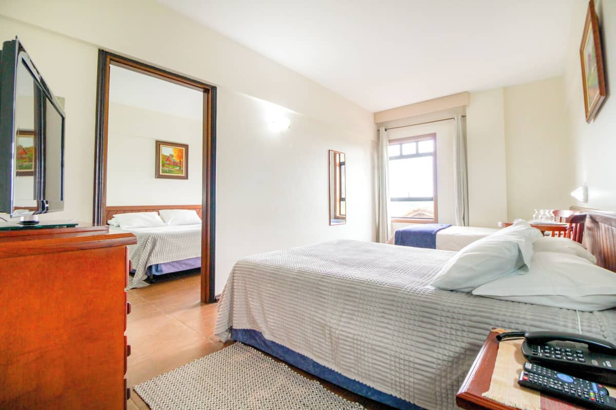 Une chambre d’hôtel avec un lit, une commode en bois, un miroir et une fenêtre avec des rideaux.