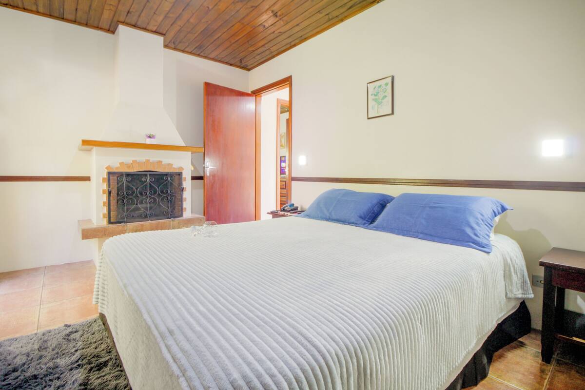 Une chambre à coucher avec un lit, un plafond en bois, une cheminée et une porte donnant sur une autre pièce.