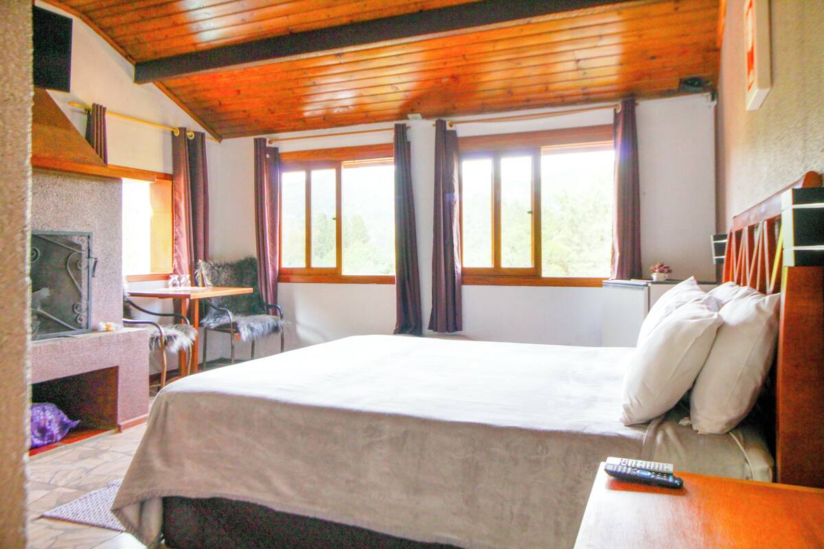 Une chambre d’hôtel avec un grand lit, un bureau avec une chaise, une cheminée et des fenêtres avec des rideaux.