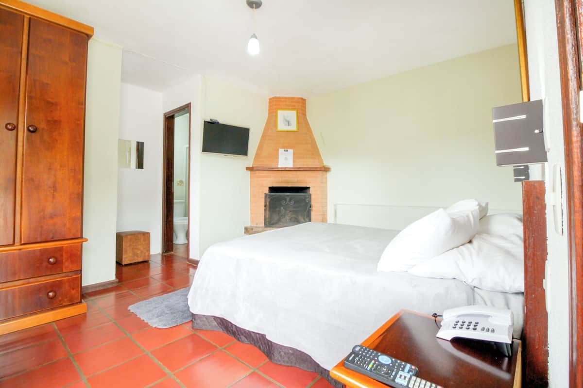 Une chambre d’hôtel comprenant un lit, une armoire en bois, une cheminée, un téléviseur et un téléphone.