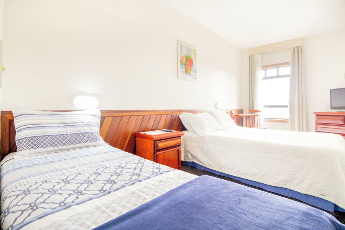 Une chambre d’hôtel avec deux lits, des têtes de lit en bois, une petite table de chevet avec une lampe, une télévision et une fenêtre avec des rideaux.