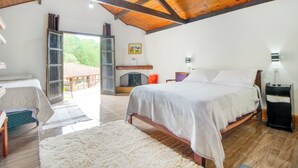 A bedroom with a large bed, a wooden ceiling, a view of the outdoors, and a small table with a lamp.