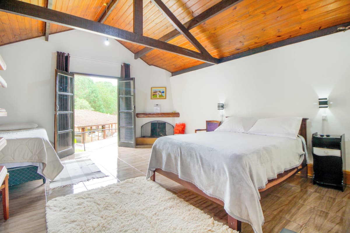 Une chambre à coucher avec un grand lit, un plafond en bois, une vue sur l’extérieur et une petite table avec une lampe.