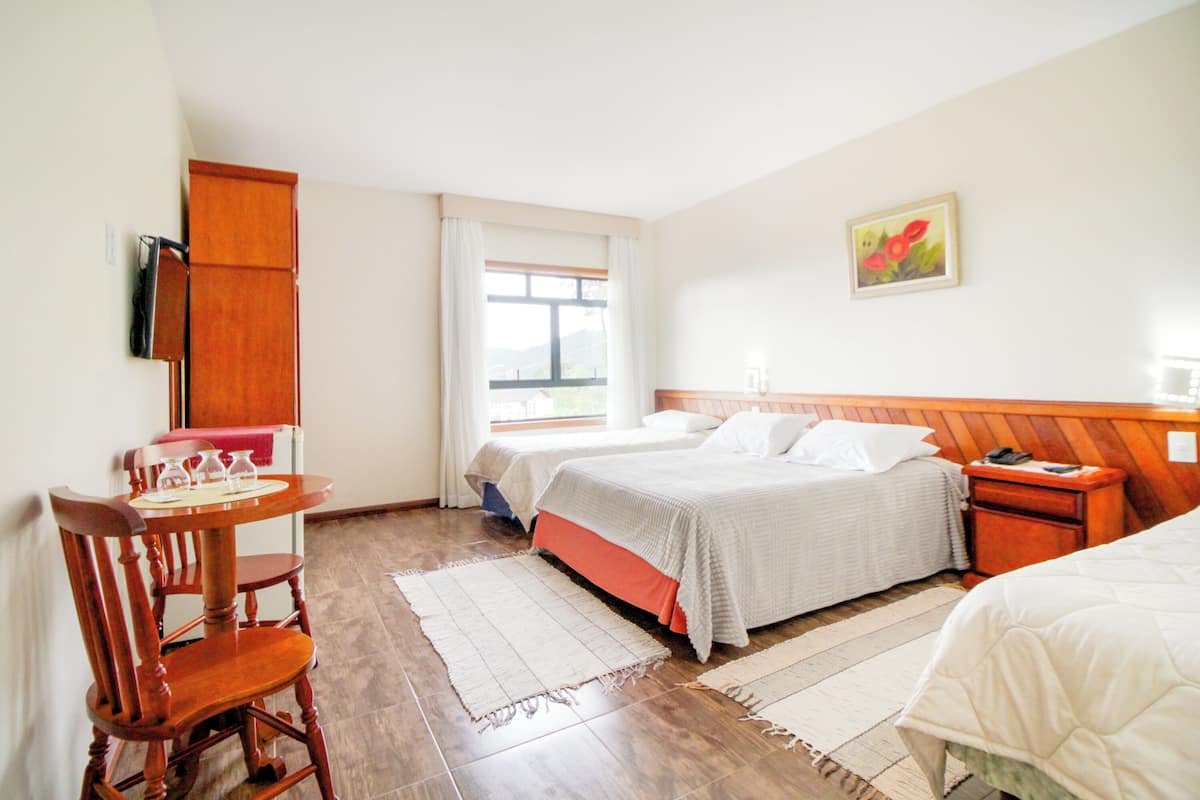 Une chambre d’hôtel avec deux lits, un bureau en bois, une chaise, une fenêtre et un tableau au mur.