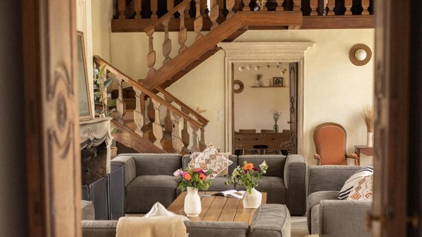 A cozy living room with a wooden staircase, grey sofas, a coffee table with vases, and a bookshelf. - La Rambolitaine . (Poigny-la-Forêt)