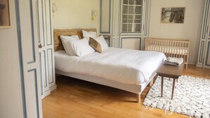 A bedroom with a bed, a wooden bench, a radiator, and a painting on the wall. - La Rambolitaine . (Poigny-la-Forêt)