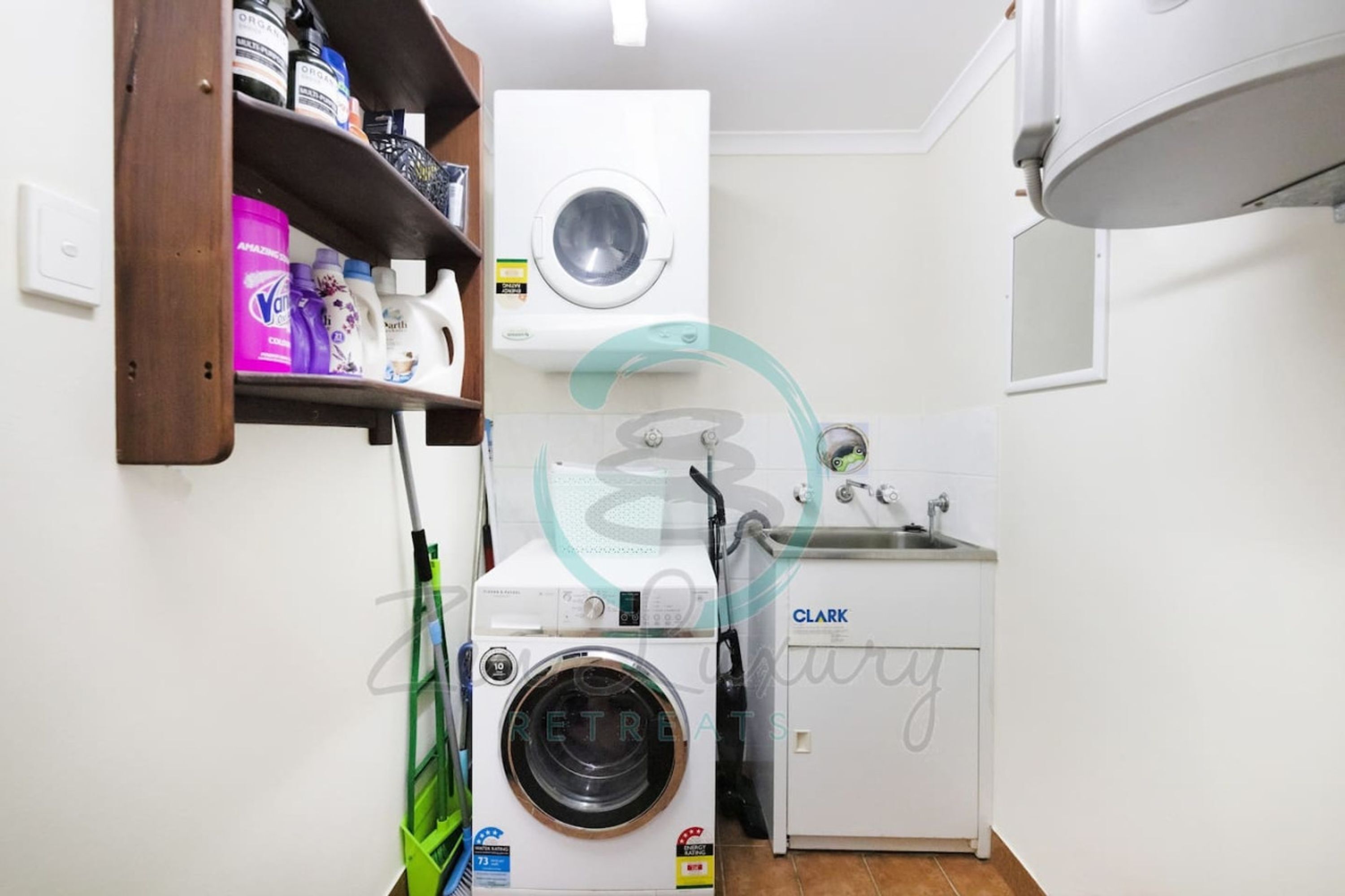 Een praktische wasruimte met een voorlader wasmachine en droger, een wasbak en planken met schoonmaakmiddelen.