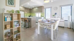 A modern kitchen with a dining area, featuring a central island, pendant lighting, and a clock on the wall. - ZEN Quest · ZEN Quest - 2bed/2bath Near Markets & Foreshore (Nightcliff)