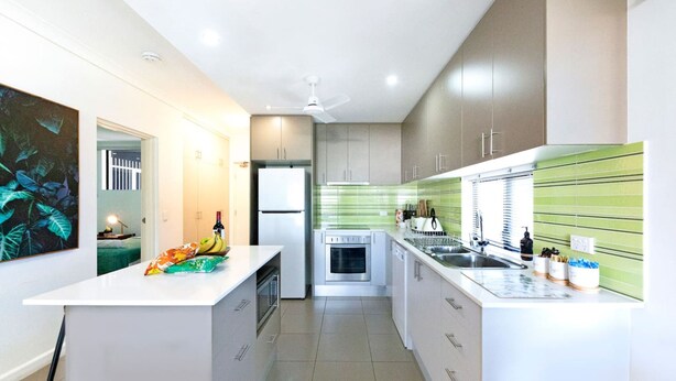 A modern kitchen with white cabinetry, a central island, and a green backsplash. - ZEN Quest · ZEN Quest - 2bed/2bath Near Markets & Foreshore (Nightcliff)