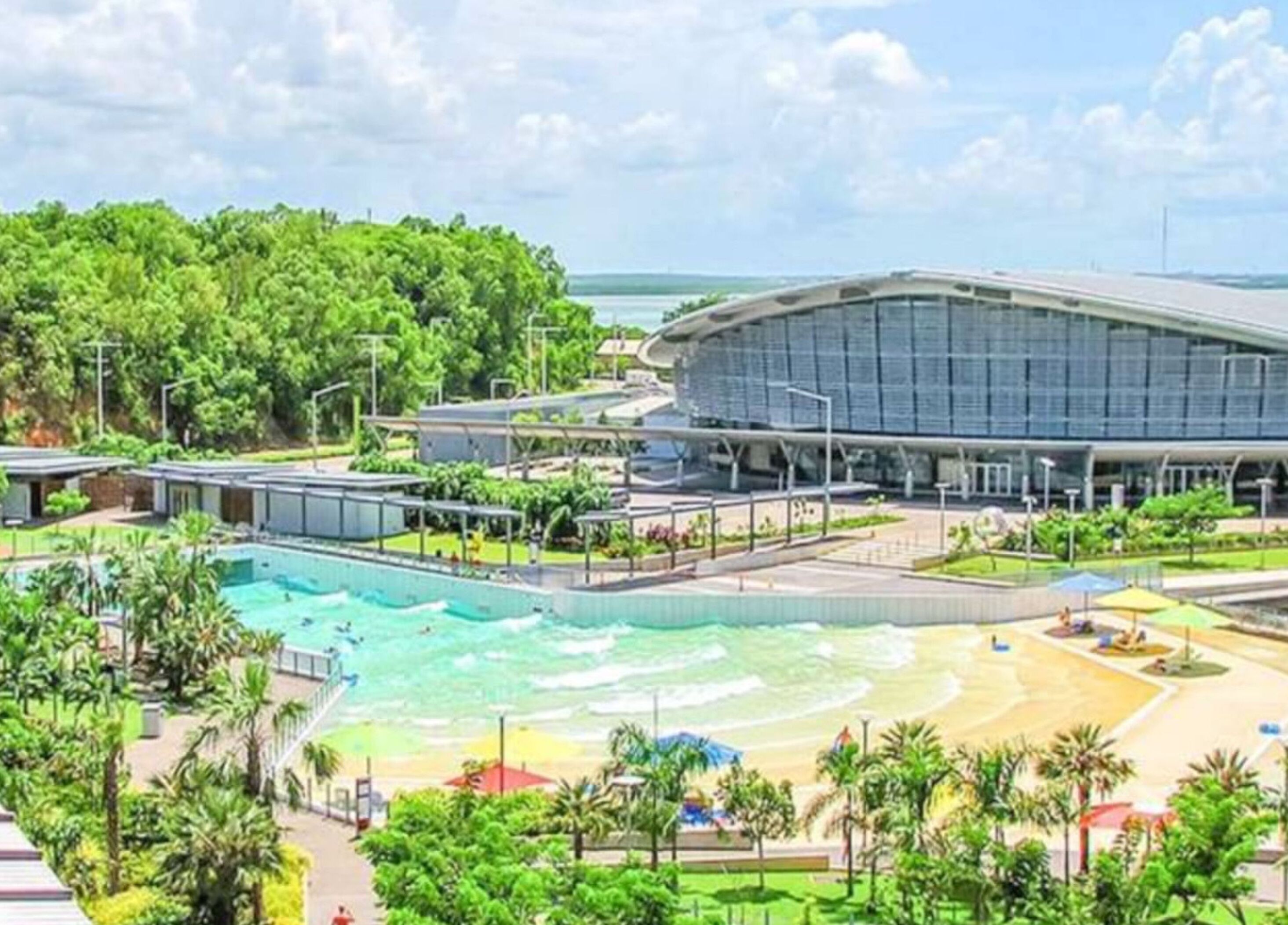 A modern hotel with a large swimming pool, a beach area, and a stadium-like structure.
