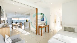 Una habitación de hotel moderna con cama, zona de estar con sofá y sillón, comedor con mesa y sillas, y un gran ventanal con vistas.