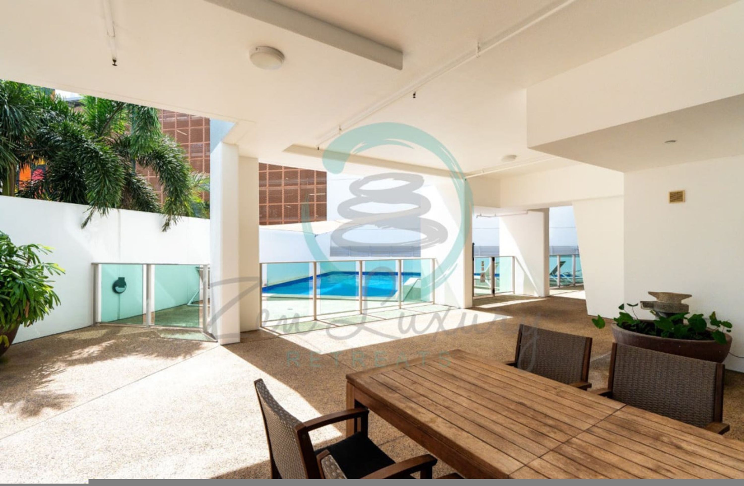 A spacious outdoor area with a wooden table and chairs, surrounded by potted plants and a view of the ocean.