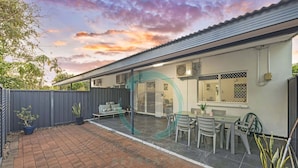 Een huis met een patio, een overdekte zithoek en een omheinde achtertuin.