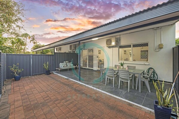 A house with a patio area, a covered seating area, and a fenced backyard.
