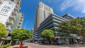 Een modern hoog gebouw met meerdere balkons en een helderblauwe lucht.