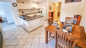 A modern kitchen with white cabinets, a black countertop, and a dining area with wooden chairs and a table set for two. - Zencity Balcony Outdoor Dining Mindal Markets (Larrakeyah)