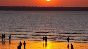 A sunset over a calm sea with silhouettes of people on the shore. - Zencity Balcony Outdoor Dining Mindal Markets (Larrakeyah)