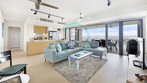 A modern living room with a sofa, coffee table, and dining area. There is a kitchen in the background with a view of the city. - ZEN Paradise - 2-br Waterfront Ocean View Retreat (Darwin)
